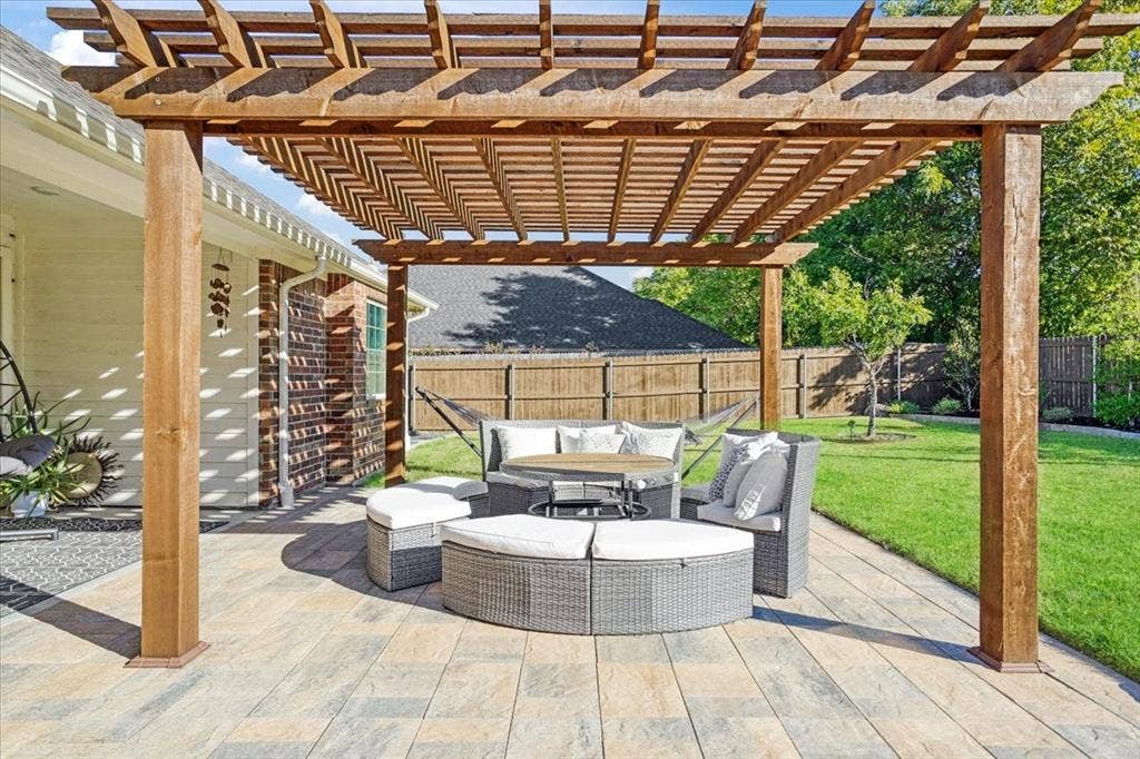 401 Mesa, Lone Oak, TX 75453 Custom wood pergola featuring a slatted roof design atop an expansive stone paver patio, complemented by a fenced backyard and brick exterior siding