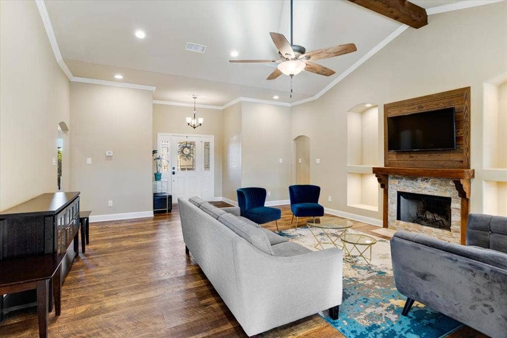 401 Mesa, Lone Oak, TX 75453 Vaulted ceiling featuring a central ceiling fan, wood-finish flooring, stone-surround fireplace with a timber mantel, and custom recessed wall niches