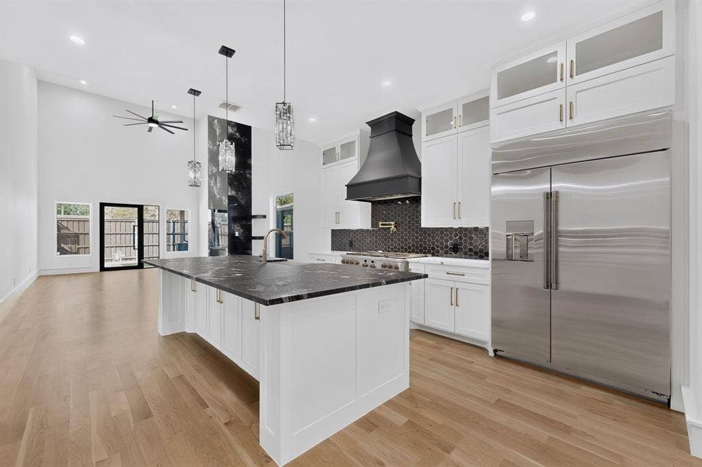 7503 Robin Road, Dallas, TX 75209 Kitchen featuring a center island with a dark stone countertop, white cabinetry with stacked uppers, a black range hood, stainless steel refrigerator, and wood-finish flooring