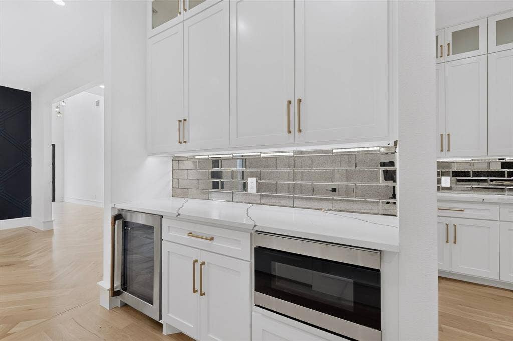 7503 Robin Road, Dallas, TX 75209 Shaker-style cabinetry with gold-toned hardware, stone-surface countertop, mirrored subway-tile backsplash, stainless steel under-counter beverage refrigerator, and drawer-style microwave