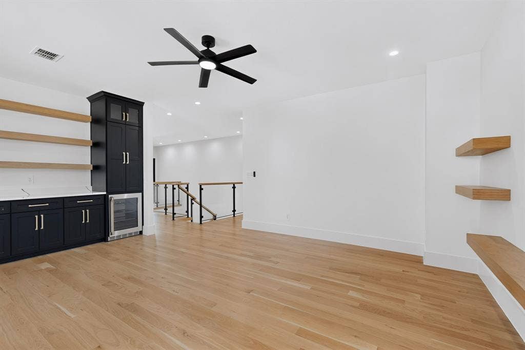 7503 Robin Road, Dallas, TX 75209 Wood-finish flooring, custom black cabinetry with built-in beverage refrigerator, natural wood floating shelves, and matte black ceiling fan