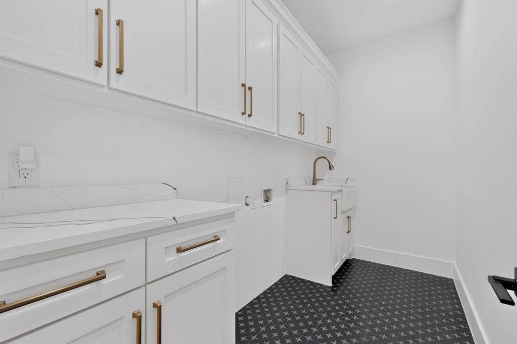 7503 Robin Road, Dallas, TX 75209 Laundry room featuring white shaker-style cabinetry, stone-finish countertops, apron-front utility sink, gold-tone hardware, and patterned tile flooring