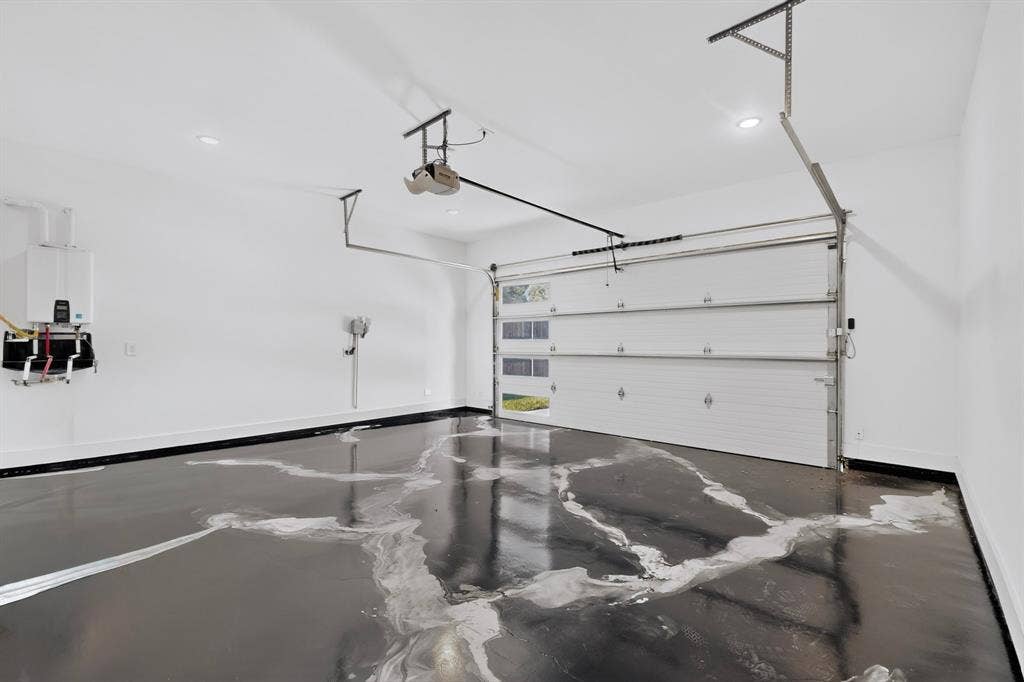7503 Robin Road, Dallas, TX 75209 Garage interior featuring high-gloss epoxy flooring, white paneled door with integrated glass windows, tankless water heater, and recessed lighting