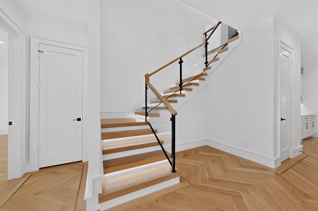 7503 Robin Road, Dallas, TX 75209 Open-riser staircase featuring wood-finish treads with integrated lighting, glass panels, a wood handrail, and black metal supports, complemented by herringbone-patterned wood-finish flooring