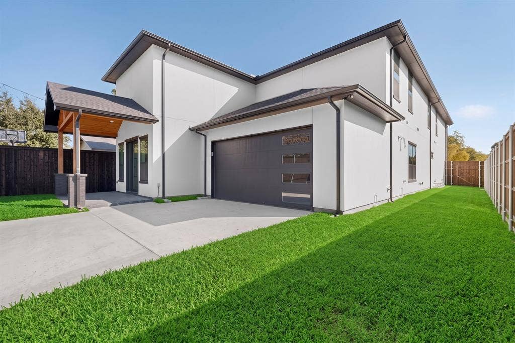 7503 Robin Road, Dallas, TX 75209 Modern exterior featuring smooth-finish siding, a multi-car garage with horizontal glass paneling, and a covered patio with wood-paneled ceiling