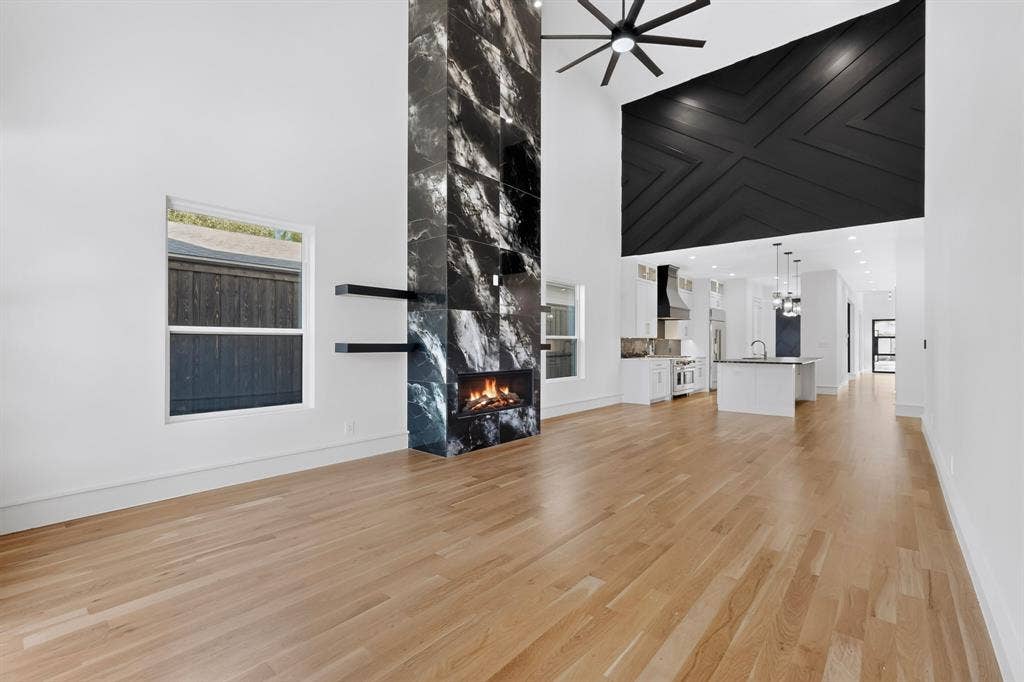 7503 Robin Road, Dallas, TX 75209 Double-height ceiling, floor-to-ceiling stone-clad fireplace, black geometric wall detailing, hardwood flooring, and large-format windows