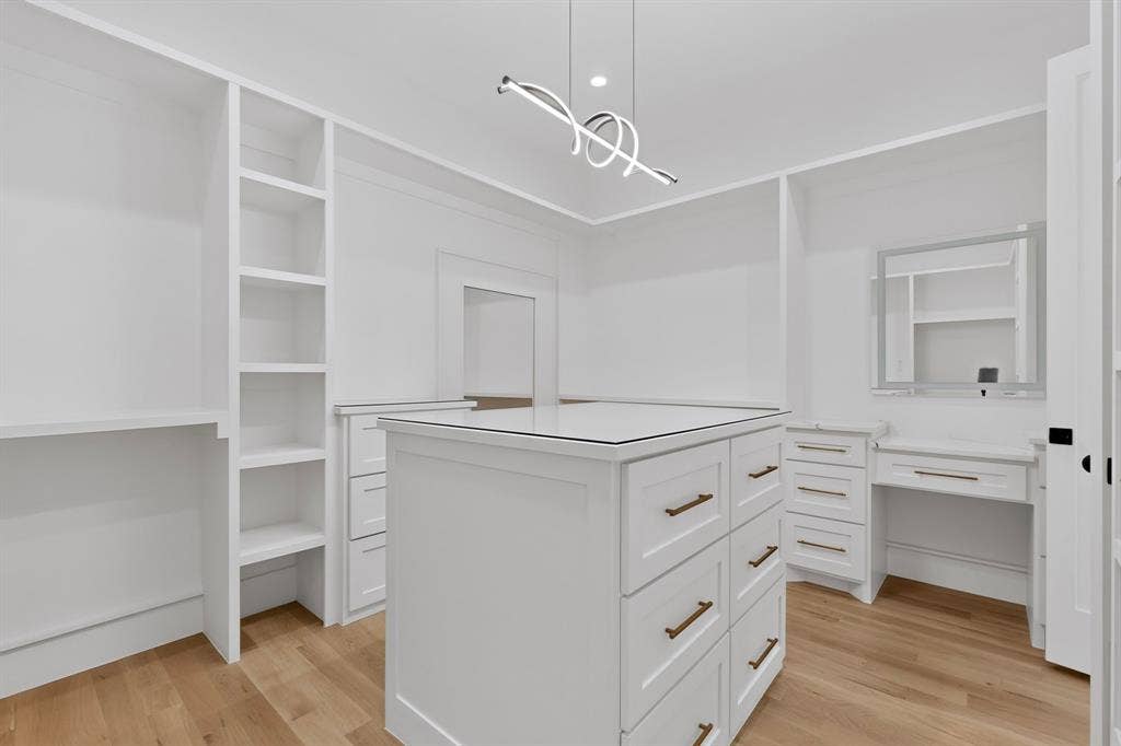 7503 Robin Road, Dallas, TX 75209 Custom walk-in closet featuring floor-to-ceiling built-in shelving, a central island with soft-close drawers, a dedicated vanity station, wood-finish flooring, and contemporary pendant lighting