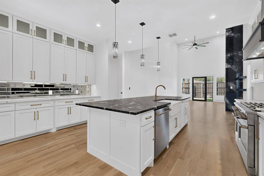 7503 Robin Road, Dallas, TX 75209 Kitchen featuring floor-to-ceiling white cabinetry, a center island with a dark stone countertop, apron-front sink, wood-finish flooring, and high-vaulted ceilings