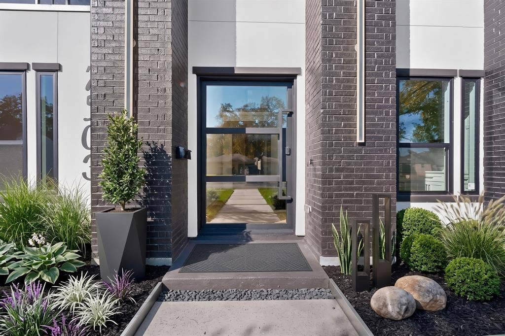 7503 Robin Road, Dallas, TX 75209 Modern entryway featuring dark brick masonry, a glass-paneled door with a geometric steel handle, vertical accent lighting, and concrete steps with black river rock detailing