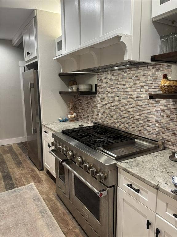 1794 County Road 4309 N, Greenville, TX 75401 Kitchen featuring a professional-grade stainless steel range with a built-in griddle, white shaker-style cabinetry, mosaic tile backsplash, stone-finish countertops, and wood-finish flooring