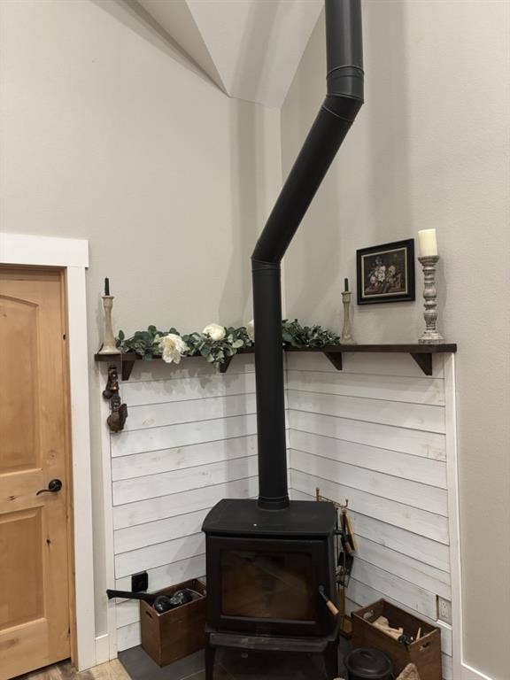 1794 County Road 4309 N, Greenville, TX 75401 Freestanding black metal stove featuring a vertical flue, white shiplap accent wall, dark-stained floating corner shelving, and a natural wood door with matching trim
