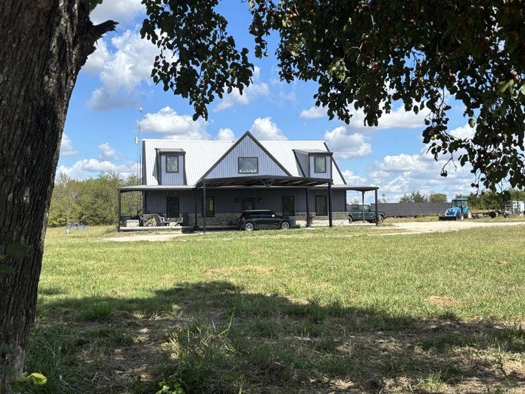 1794 County Road 4309 N, Greenville, TX 75401 Barndominium-style exterior featuring metal siding, stone veneer accents, a standing seam metal roof, dormer windows, and an expansive covered porch