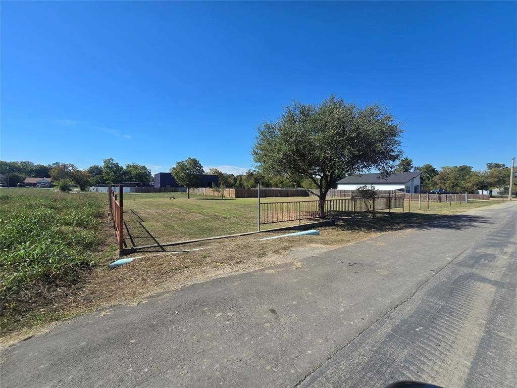 Cleared lot featuring a level grass landscape, perimeter metal fencing, and mature trees