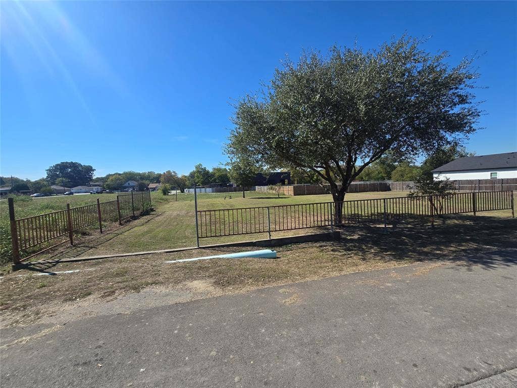 Open lot featuring a fenced perimeter, expansive lawn, and mature tree