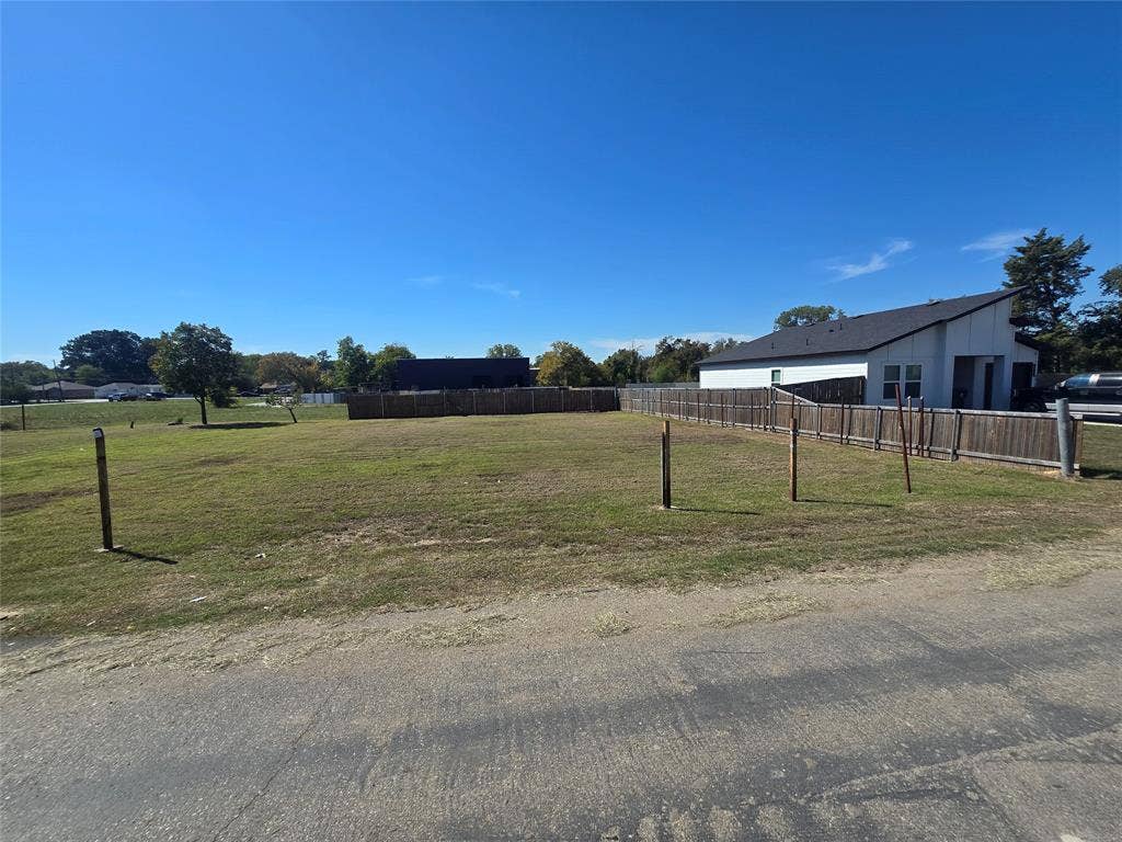 Cleared residential lot featuring a level grass landscape, paved street access, and perimeter wood fencing