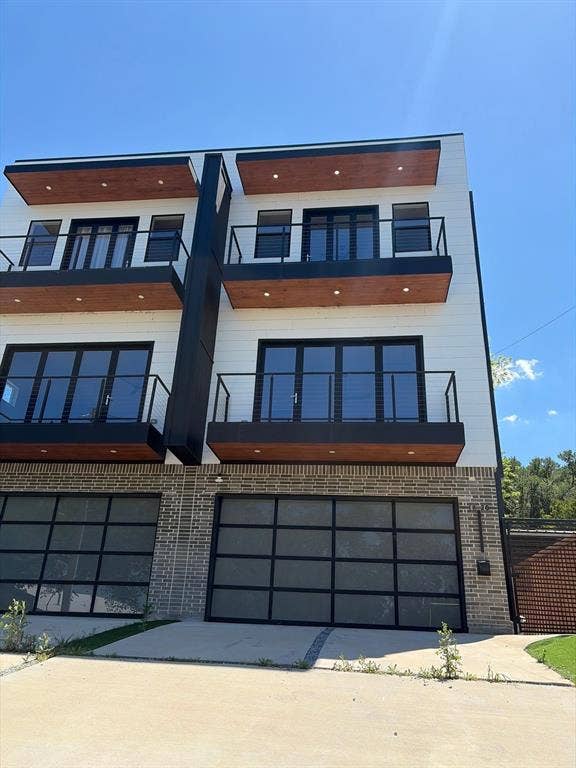 1820 Pollard Street, Dallas, TX 75208 Contemporary exterior featuring white horizontal siding, brick masonry, wood-finish balcony soffits, integrated recessed lighting, and glass-paneled garage doors