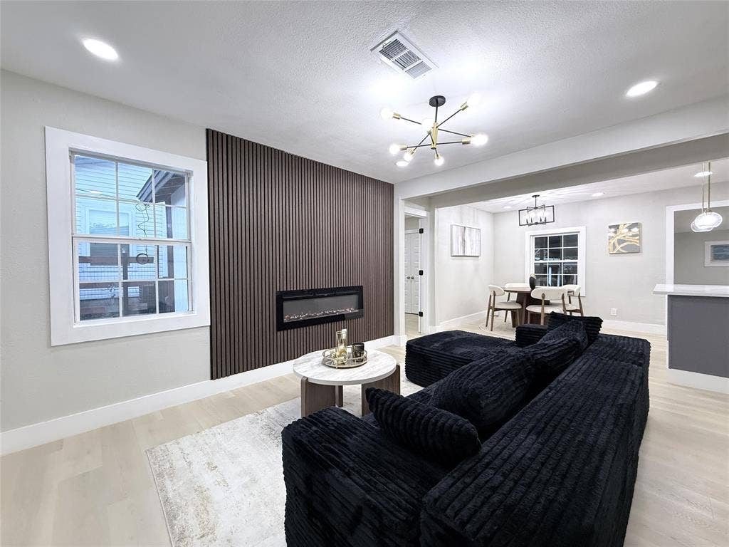 4522 Idaho Avenue, Dallas, TX 75216 Vertical wood-slat accent wall featuring a recessed electric fireplace, multi-arm modern light fixture, and wood-finish flooring