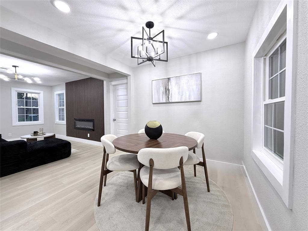 4522 Idaho Avenue, Dallas, TX 75216 Open-concept interior featuring wood-finish flooring, a contemporary geometric chandelier, a floor-to-ceiling dark wood accent wall, and a built-in linear fireplace