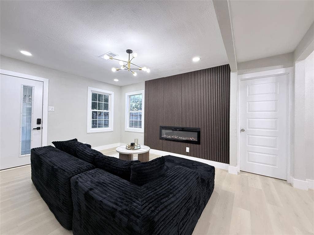 4522 Idaho Avenue, Dallas, TX 75216 Vertical slat accent wall with a linear electric fireplace, modern multi-arm chandelier, light-toned wood-finish flooring, and multi-pane windows