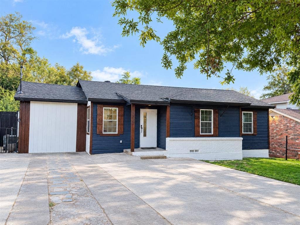 4522 Idaho Avenue, Dallas, TX 75216 Single-story exterior featuring navy horizontal siding, contrasting white brick accents, dark-stained wood shutters, a covered front entry, and an attached garage