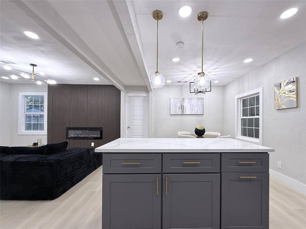 4522 Idaho Avenue, Dallas, TX 75216 Kitchen island with quartz countertop and dark cabinetry featuring brass hardware, accented by glass pendant lighting, recessed ceiling lights, and an electric fireplace set within a vertical-slat accent wall