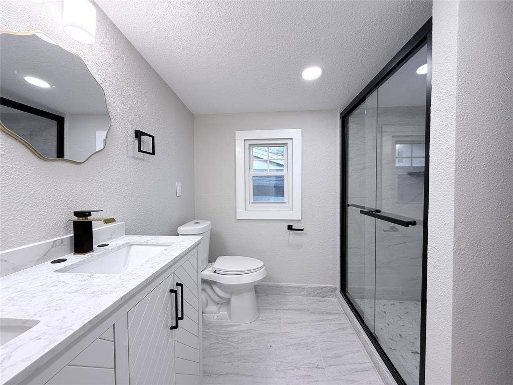 4522 Idaho Avenue, Dallas, TX 75216 Bathroom featuring a dual-sink vanity with light stone-patterned countertops, walk-in shower with matte black fixtures and a glass enclosure, and patterned tile flooring