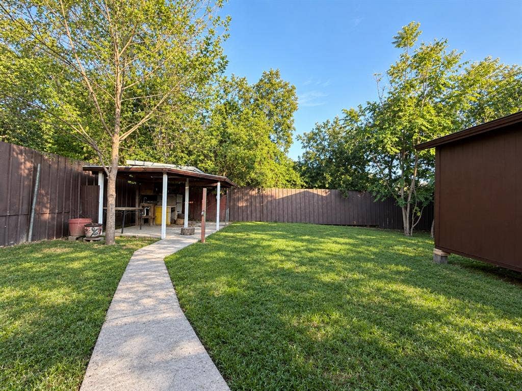 4522 Idaho Avenue, Dallas, TX 75216 Fenced backyard featuring a manicured lawn, concrete walkway, covered patio structure, and mature trees