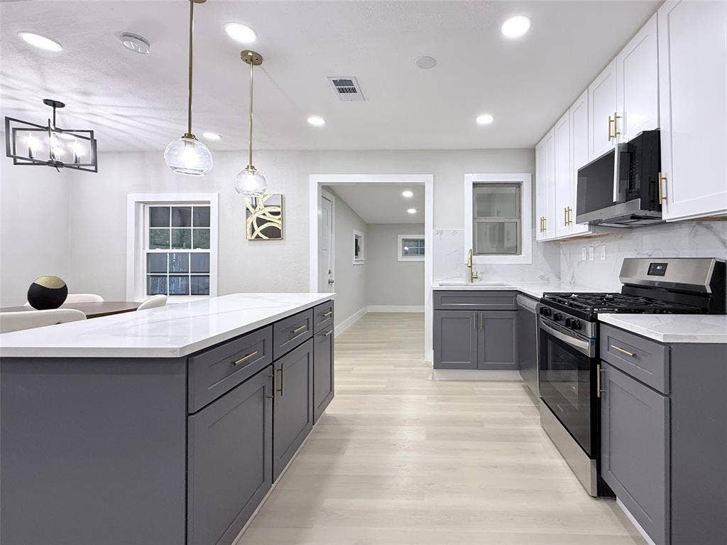 4522 Idaho Avenue, Dallas, TX 75216 Kitchen featuring a large central island, white quartz countertops, dual-tone shaker cabinetry, wood-finish flooring, and pendant lighting