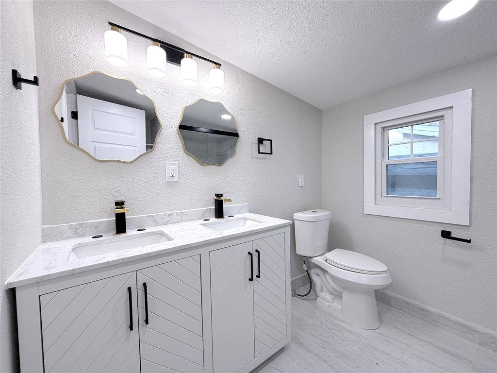 4522 Idaho Avenue, Dallas, TX 75216 Double vanity with stone-look countertop, integrated dual sinks, chevron-patterned cabinetry, matte black hardware, and two scalloped-edge mirrors