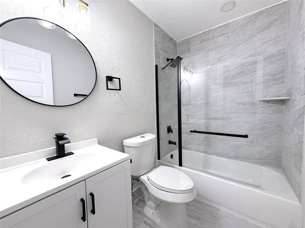 4522 Idaho Avenue, Dallas, TX 75216 Bathroom featuring a white vanity with a matte black faucet, oval wall-mounted mirror, and a glass-enclosed shower-tub combination with horizontal tile surround and matte black fixtures