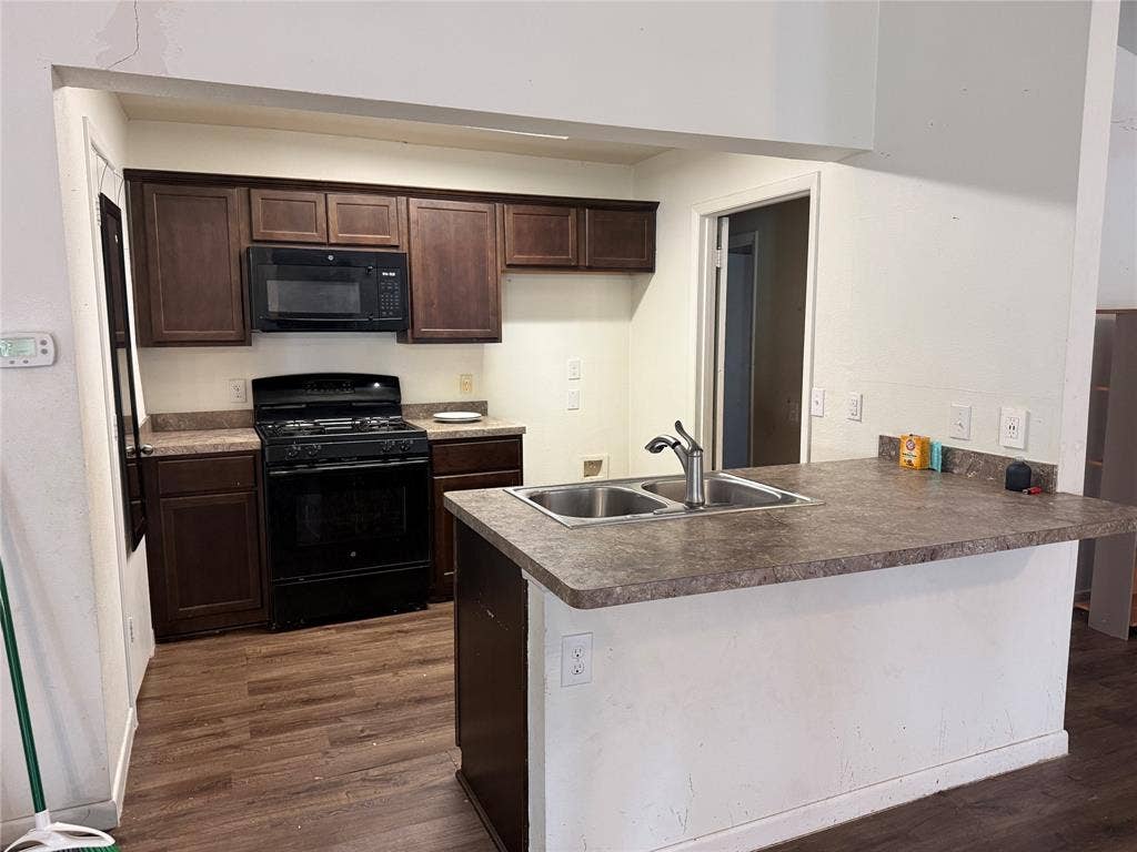 3825 Eugene Court N, Irving, TX 75062 Kitchen featuring dark wood cabinetry, laminate countertops, a dual-basin stainless steel sink with a high-arch faucet, black appliance suite, and wood-finish flooring