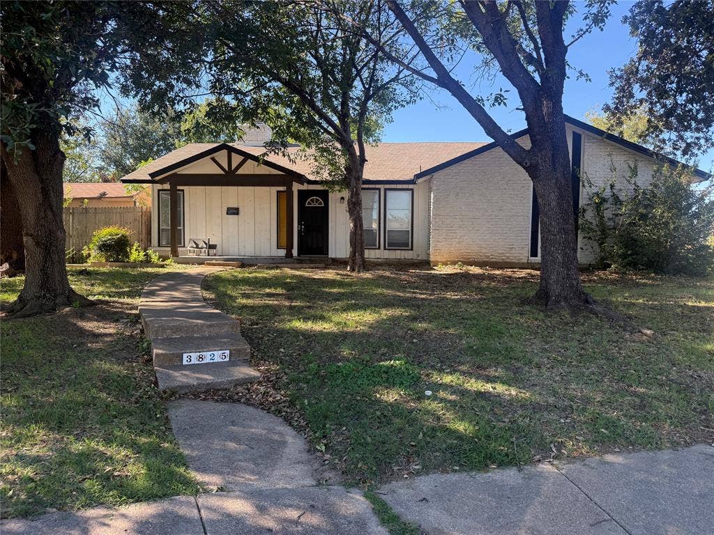 3825 Eugene Court N, Irving, TX 75062 Single-story residence featuring a painted brick and vertical siding exterior, decorative wood gable truss, covered front porch, and mature trees