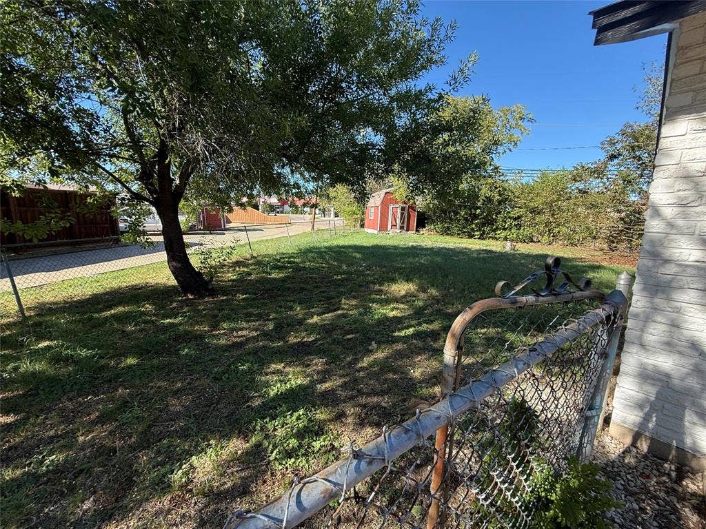 3825 Eugene Court N, Irving, TX 75062 Expansive yard featuring mature trees, a chain-link fence, and a detached storage structure