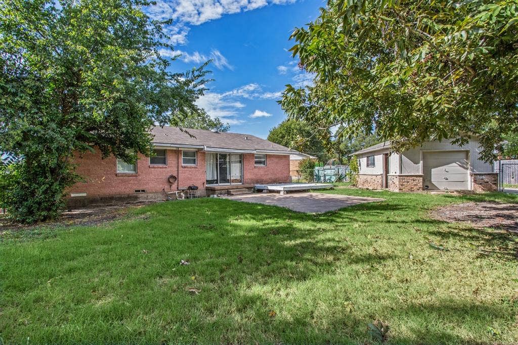 1220 Colfax Circle, Richardson, TX 75080 Exterior featuring brick cladding, a detached garage, a paved patio area, and mature trees on the lot