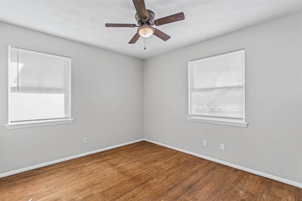 1220 Colfax Circle, Richardson, TX 75080 Neutral-toned interior space featuring wood-finish flooring, two dual-pane windows with integrated blinds, and a central ceiling fan with an integrated light fixture