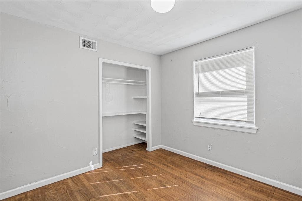 1220 Colfax Circle, Richardson, TX 75080 Room featuring wood-finish flooring, neutral wall paint, and a recessed closet with built-in shelving