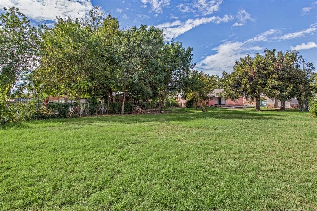 1220 Colfax Circle, Richardson, TX 75080 Expansive backyard featuring a large grass lawn, mature trees, and perimeter chain-link fencing