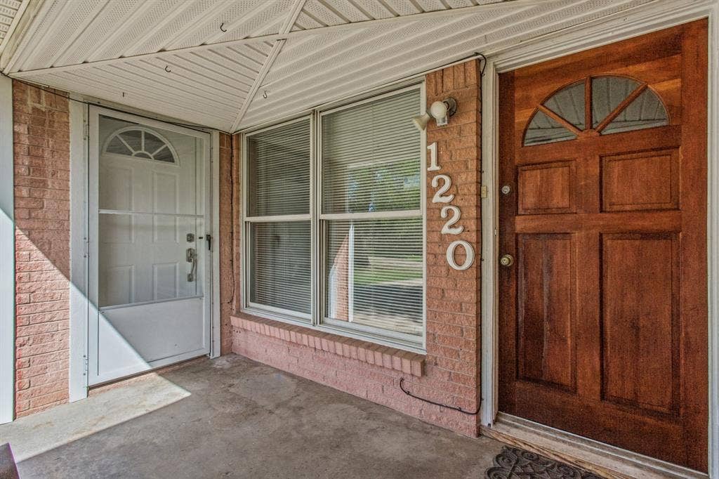 1220 Colfax Circle, Richardson, TX 75080 Covered entryway featuring a brick facade, solid wood entry door with a semi-circular transom window, secondary storm door, and large multi-pane windows