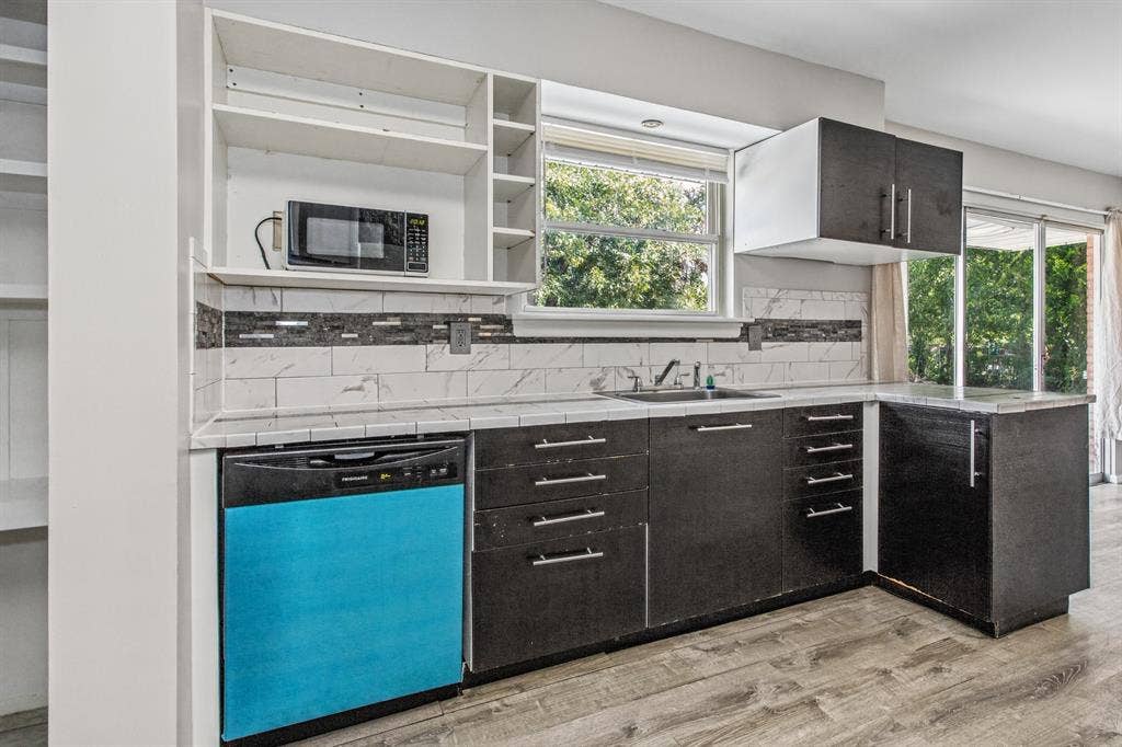 1220 Colfax Circle, Richardson, TX 75080 Kitchen featuring dark cabinetry, stone-pattern tile backsplash, wood-finish flooring, integrated dishwasher, and open shelving