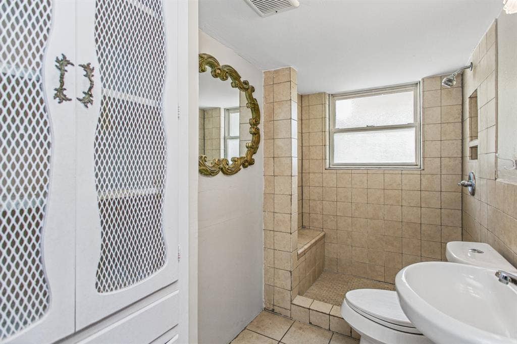 1220 Colfax Circle, Richardson, TX 75080 Bathroom featuring a walk-in tile shower with an integrated bench, built-in floor-to-ceiling storage cabinetry with wire mesh door panels, and neutral-toned wall and floor tiling