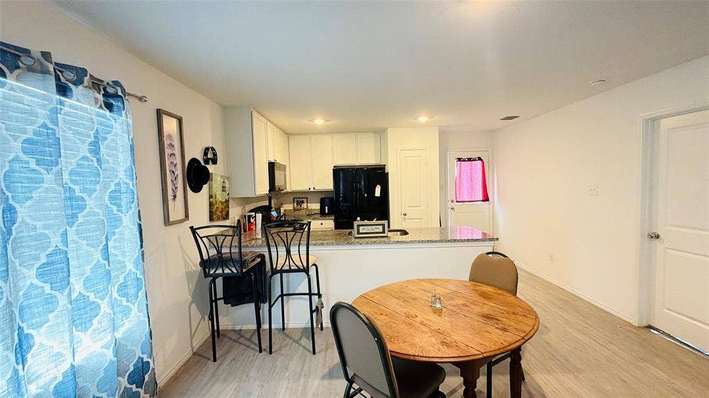 Kitchen area featuring white cabinetry, stone-finish countertops, integrated breakfast bar, and wood-finish flooring