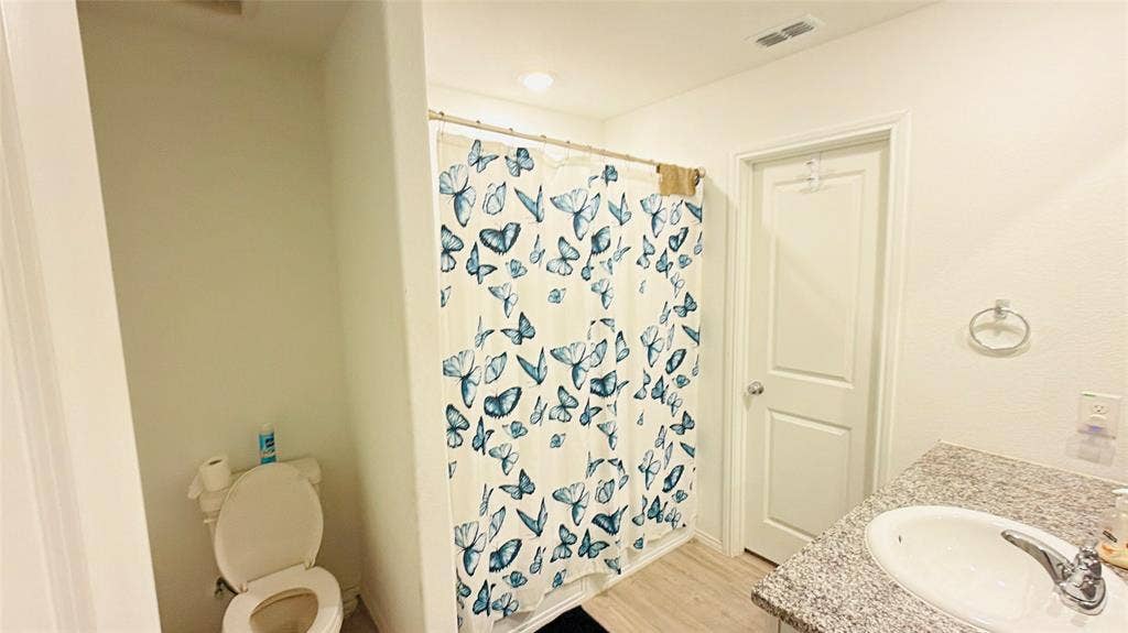 Bathroom featuring a vanity with a stone-finish countertop, undermount sink, chrome faucet, and wood-finish flooring