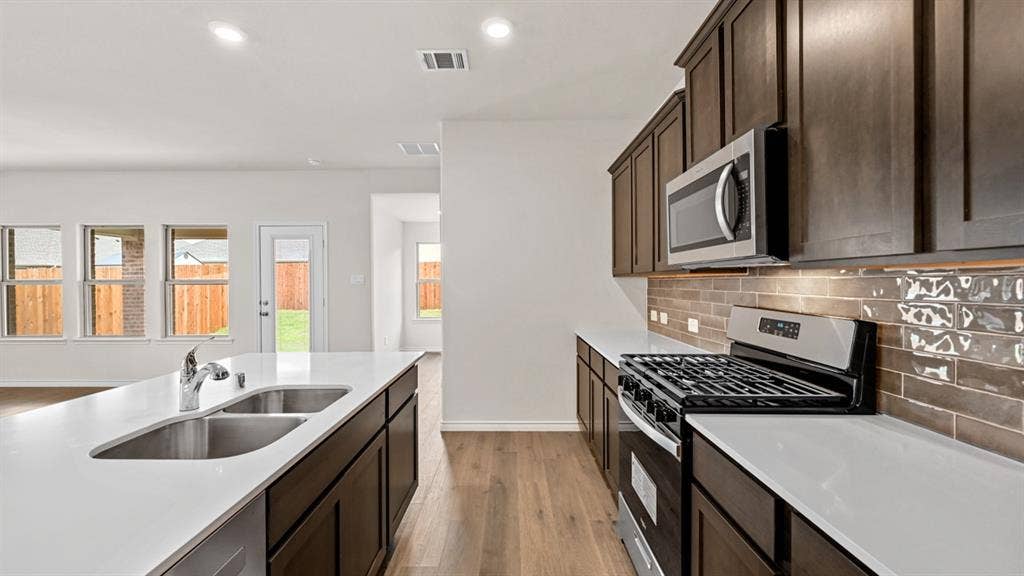 Kitchen featuring dark wood-finish cabinetry, stainless steel appliances, white countertops, and a subway tile backsplash