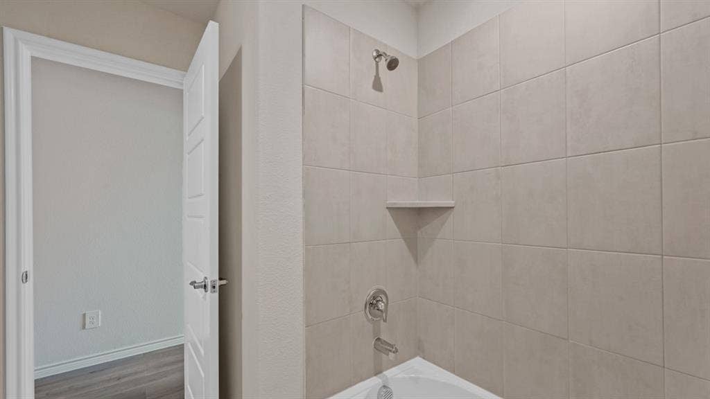 Shower/tub combination with light-toned rectangular tile surround, built-in corner shelf, and chrome fixtures