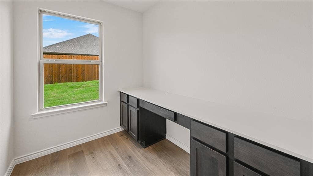 Integrated desk with dark wood-finish cabinetry and light-toned countertop, wood-finish flooring, and a window with white trim