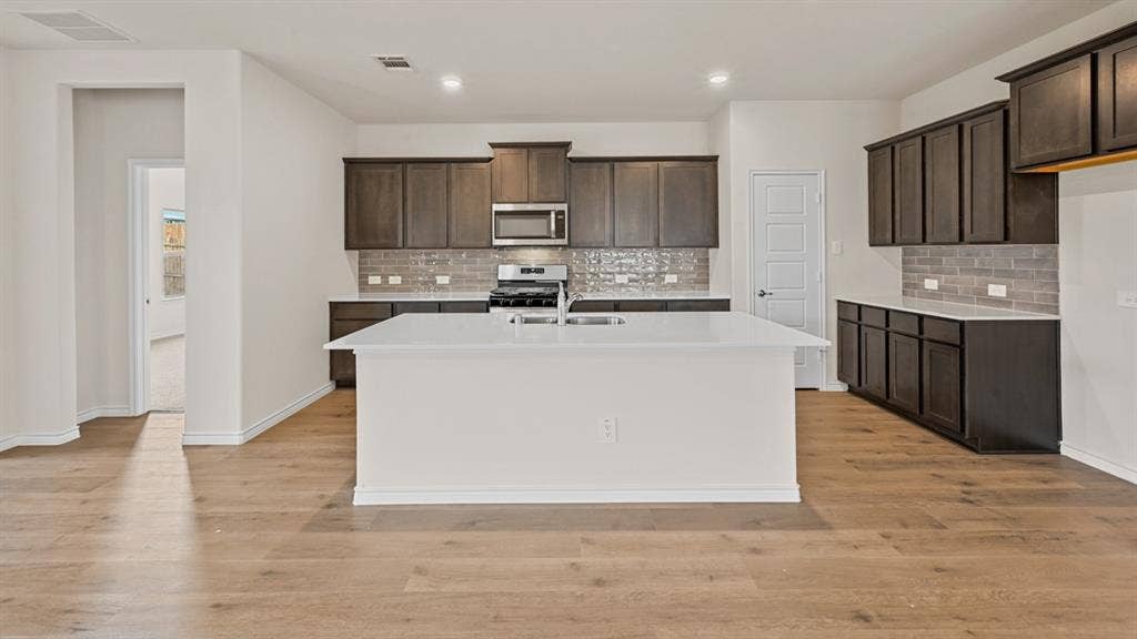 Spacious kitchen with a central island, dark wood-finish cabinetry, light-toned countertops, and a subway tile backsplash