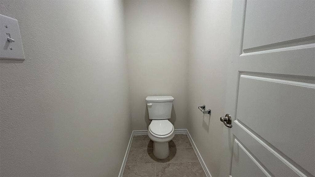 410 Campfield Drive, Caddo Mills, TX 75135 Neutral-toned restroom featuring a white toilet, tiled flooring, and a paneled interior door with metallic hardware