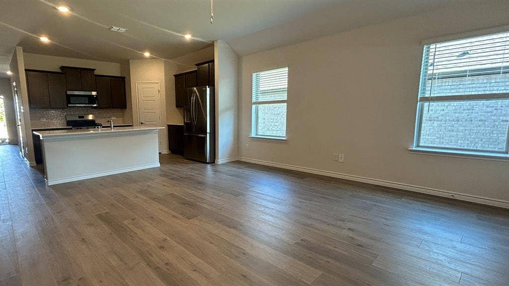 410 Campfield Drive, Caddo Mills, TX 75135 Open-concept interior featuring wood-finish flooring, recessed lighting, and a kitchen with dark cabinetry, stainless steel appliances, and a quartz-topped peninsula