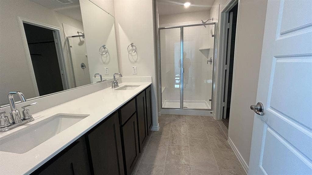 410 Campfield Drive, Caddo Mills, TX 75135 Bathroom featuring dual vanity with stone-composite countertop, dark wood cabinetry, large vanity mirror, and glass-enclosed shower with tiled flooring