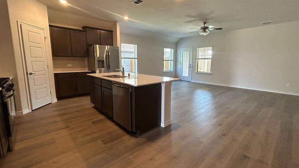 410 Campfield Drive, Caddo Mills, TX 75135 Kitchen featuring dark wood-finish cabinetry, a central island with a stone-surface countertop, stainless steel appliances, and wood-finish flooring